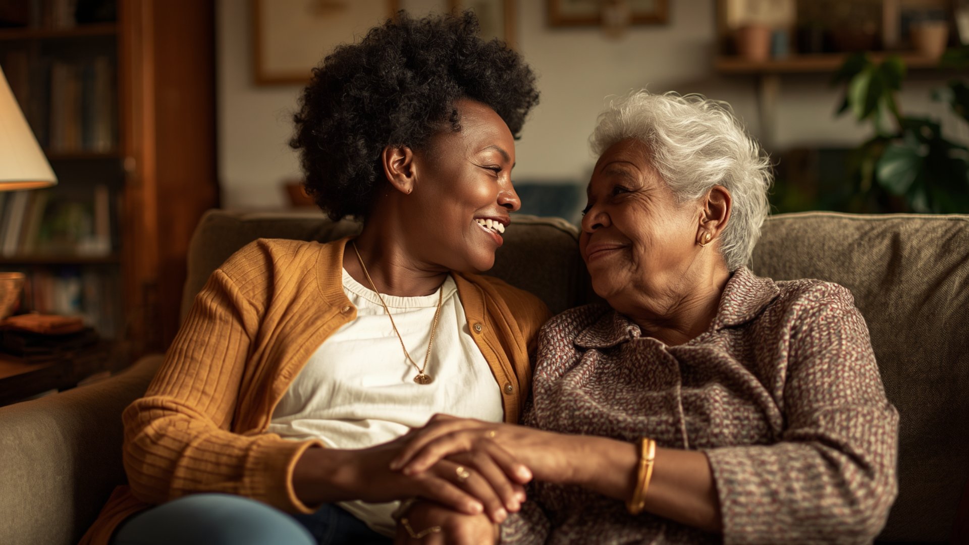 Black woman and elderly mother holding hands warmly on a sofa